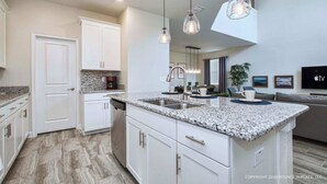A modern kitchen with granite countertops, white cabinetry, and pendant lighting. - Chic Home, Themed Bedrooms, Game Room, Best Spot (Kissimmee)