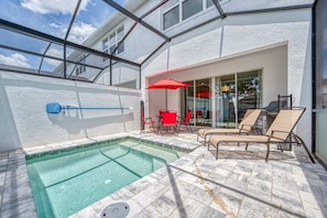 A swimming pool with lounge chairs and a table, a glass door leading inside, and a clear sky.