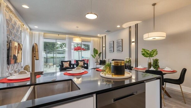 Una cocina moderna con una isla central, electrodomésticos de acero inoxidable y un comedor con manteles individuales rojos y sillas negras.