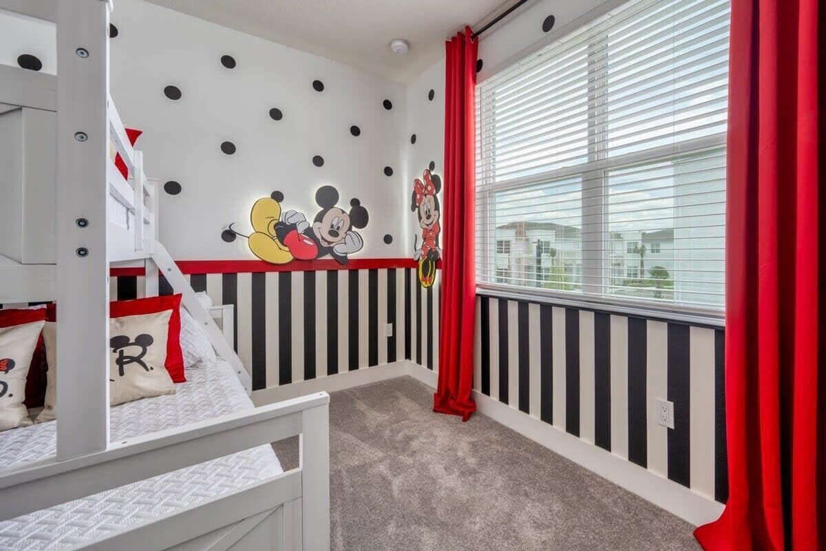 Een kinderkamer met een stapelbed, een Mickey Mouse muurstickerset en een raam met zonwering.