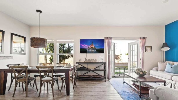 Ein geräumiges Wohnzimmer mit Essbereich, einem an der Wand befestigten Fernseher und Blick ins Freie durch große Fenster.