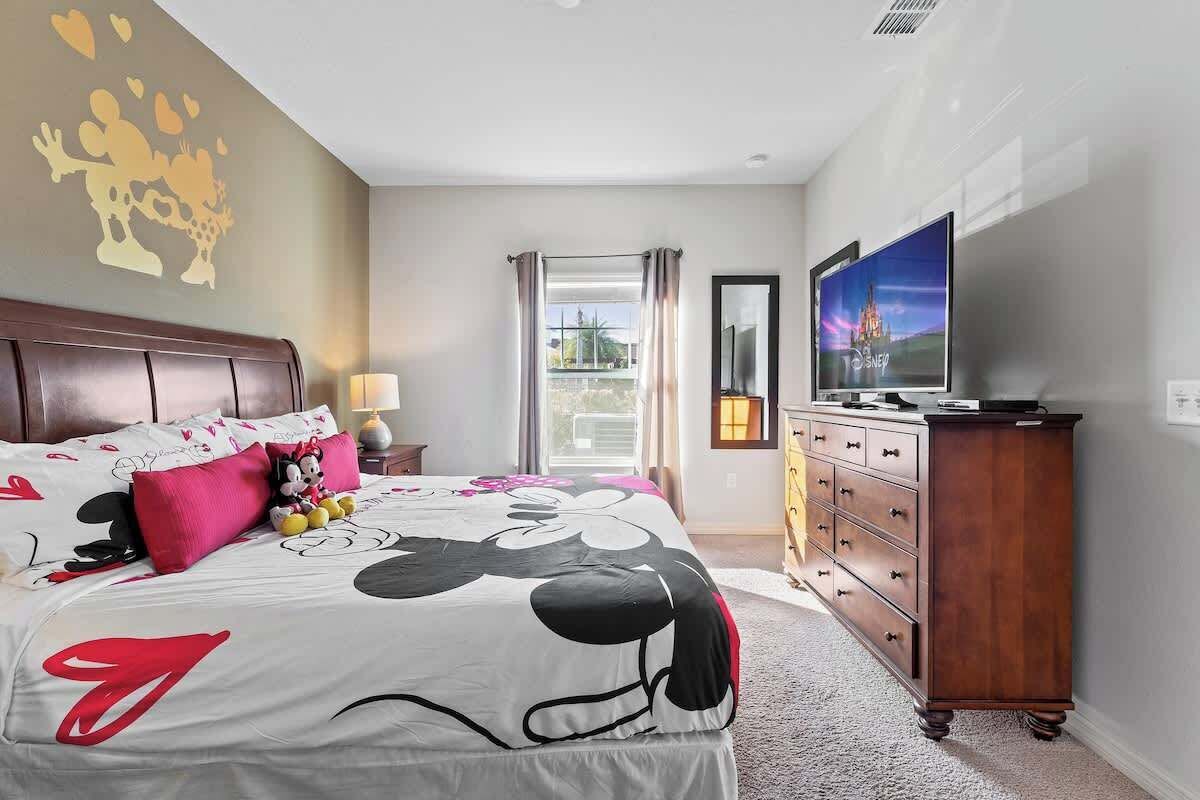 A hotel room with a bed, a television, a dresser, and a balcony with curtains.