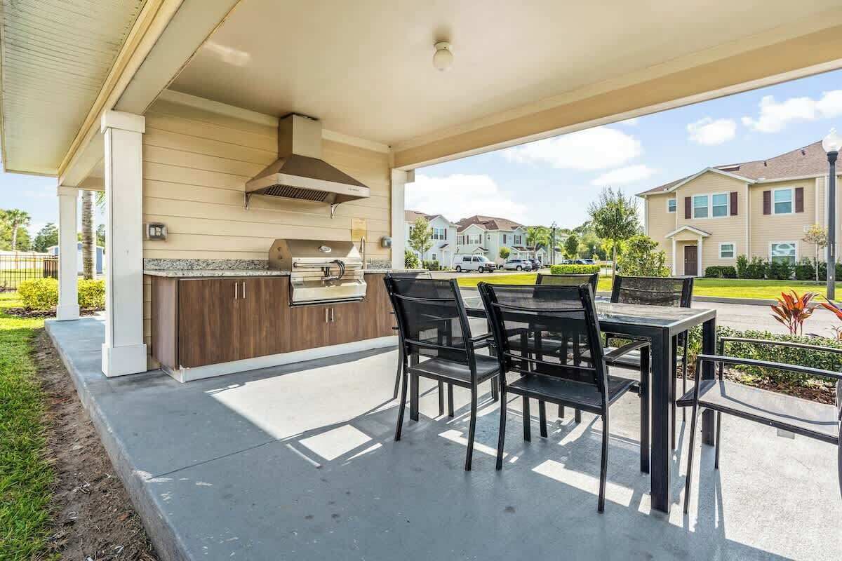 An outdoor patio with a grill, seating area, and a view of residential buildings.