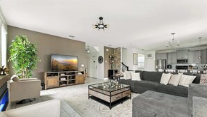A modern living room with a glass coffee table, grey sofas, and a large flat-screen TV. - Luxury Decor 6BR at Storey Lake Sleeps 16 (Kissimmee)