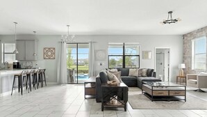 A spacious living area with a sofa, coffee table, and bar stools. There is a large window providing a view of the outdoors. - Luxury Decor 6BR at Storey Lake Sleeps 16 (Kissimmee)