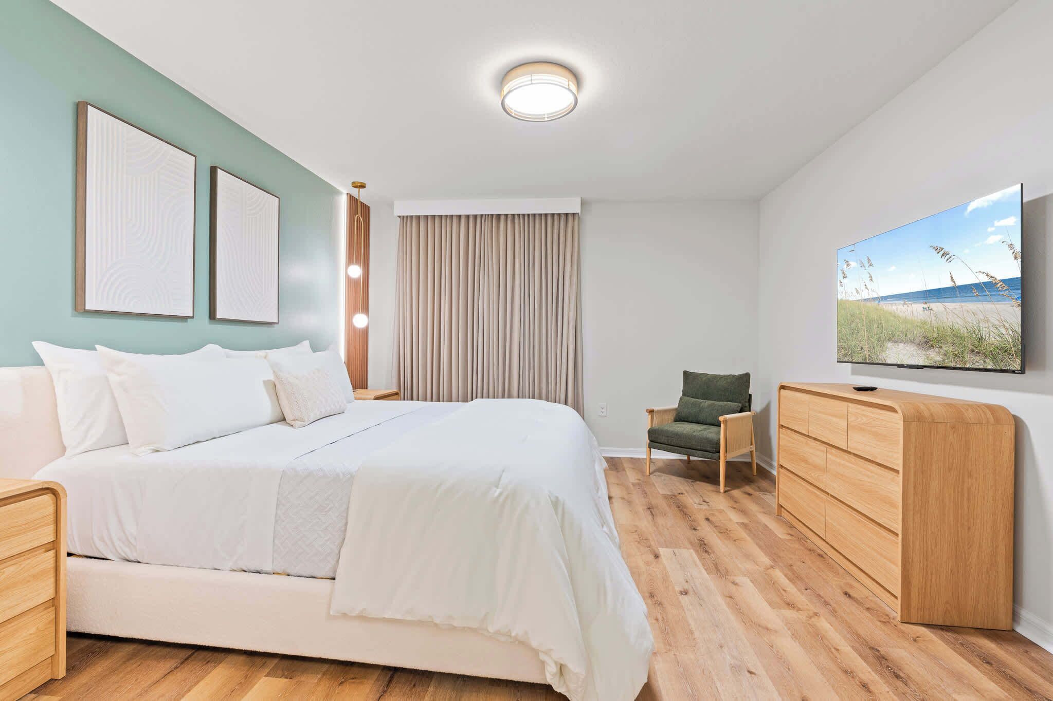 Ein modernes Schlafzimmer mit einem großen Bett, einer Holzkommode, einem Fernseher und Kunstwerken an den Wänden.