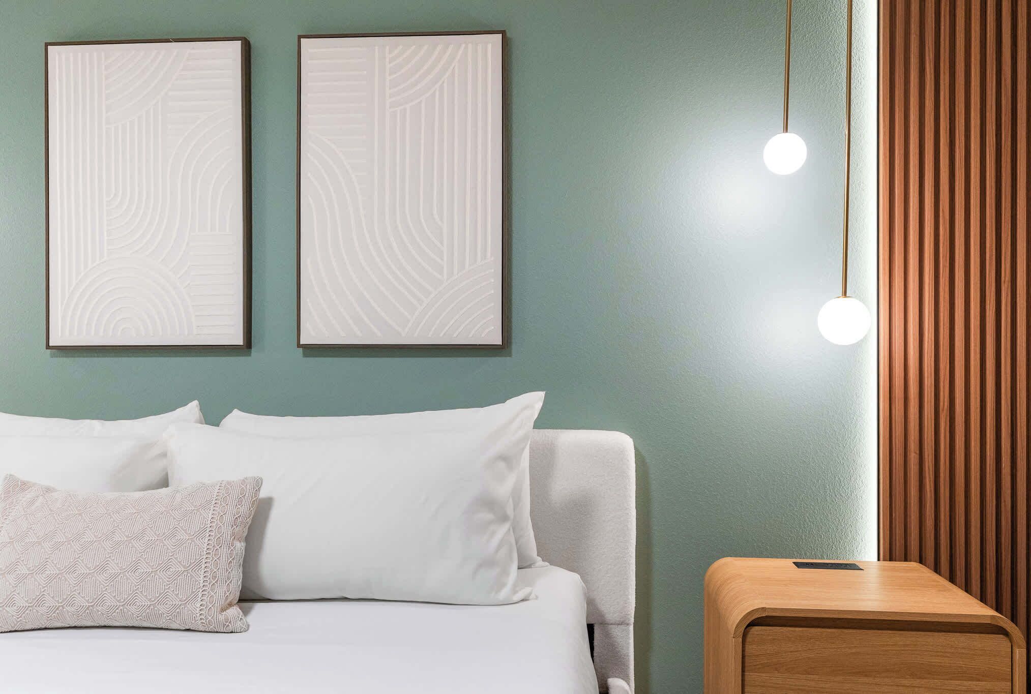 A neatly arranged bedroom with a bed, pillows, a bedside table, and two wall-mounted picture frames.