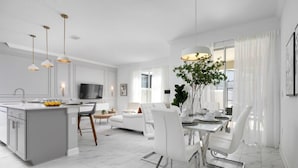 A modern kitchen with a central island, dining area with white chairs, and a TV mounted on the wall. - Chic Retreat - Unforgettable Stay (Kissimmee)