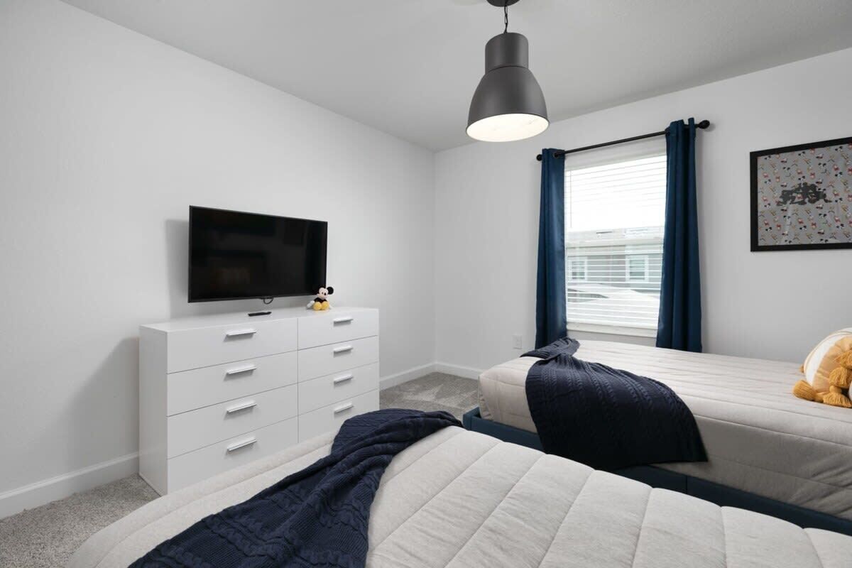 A bedroom with a bed, a dresser, a television, and a window with curtains.