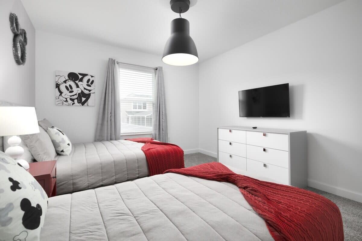 A bedroom with two beds, a TV, a dresser, and a window with curtains.