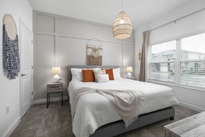 A modern bedroom with a large bed, bedside lamps, a hanging light fixture, and a view of the outside through a window. - Chic Modern Home- Mickey & Star Wars Magic (Davenport)