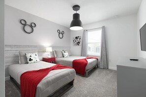 A modern bedroom with two beds, a red throw blanket, a desk with a TV, and wall art. - Chic Modern Home- Mickey & Star Wars Magic (Davenport)