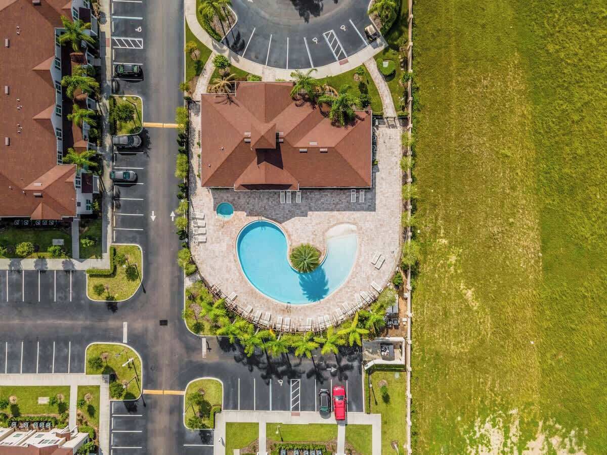 An aerial view of a property with a swimming pool, parking lots, and surrounding greenery.