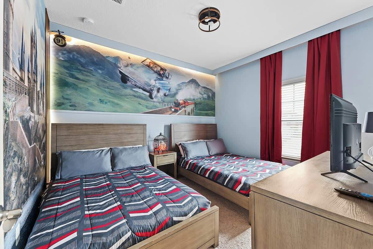 Une chambre d’hôtel avec deux lits, un bureau, une télévision et une fresque représentant un train sur le mur.