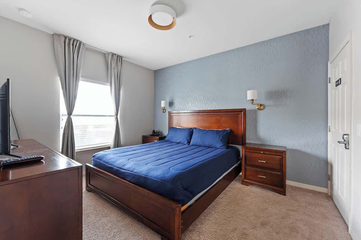 Une chambre avec un grand lit, un bureau, une table de chevet et une lampe.
