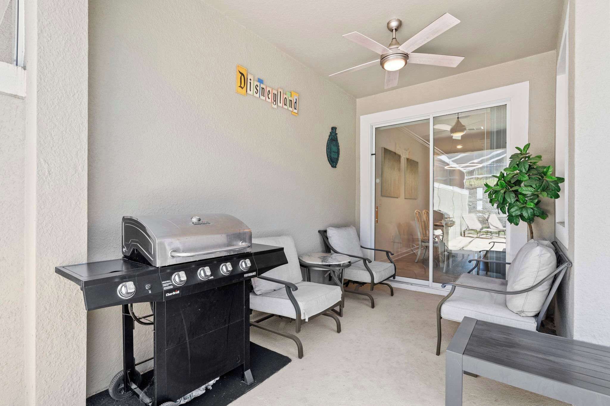A patio with a grill, chairs, and a ceiling fan.
