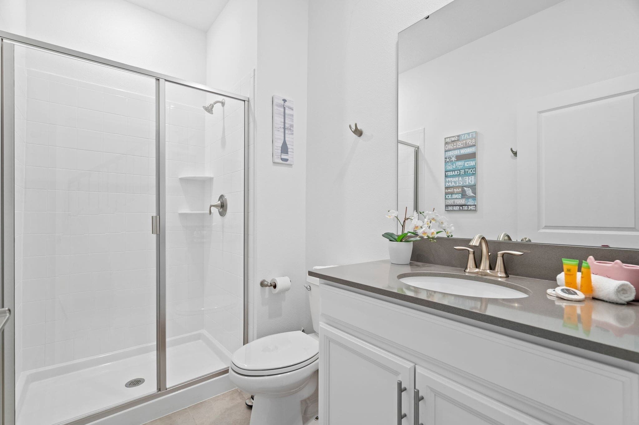 Un baño moderno con cabina de ducha de vidrio, inodoro, lavabo con espejo y una orquídea en maceta.