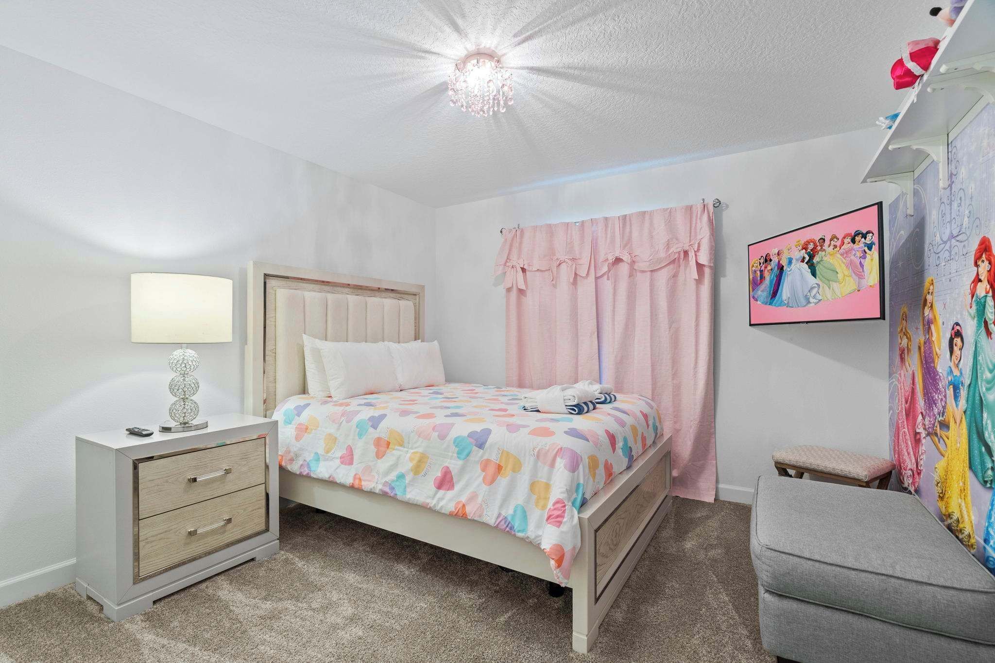 Un dormitorio con cama, mesita de noche, lámpara y un cartel de una princesa Disney en la pared.