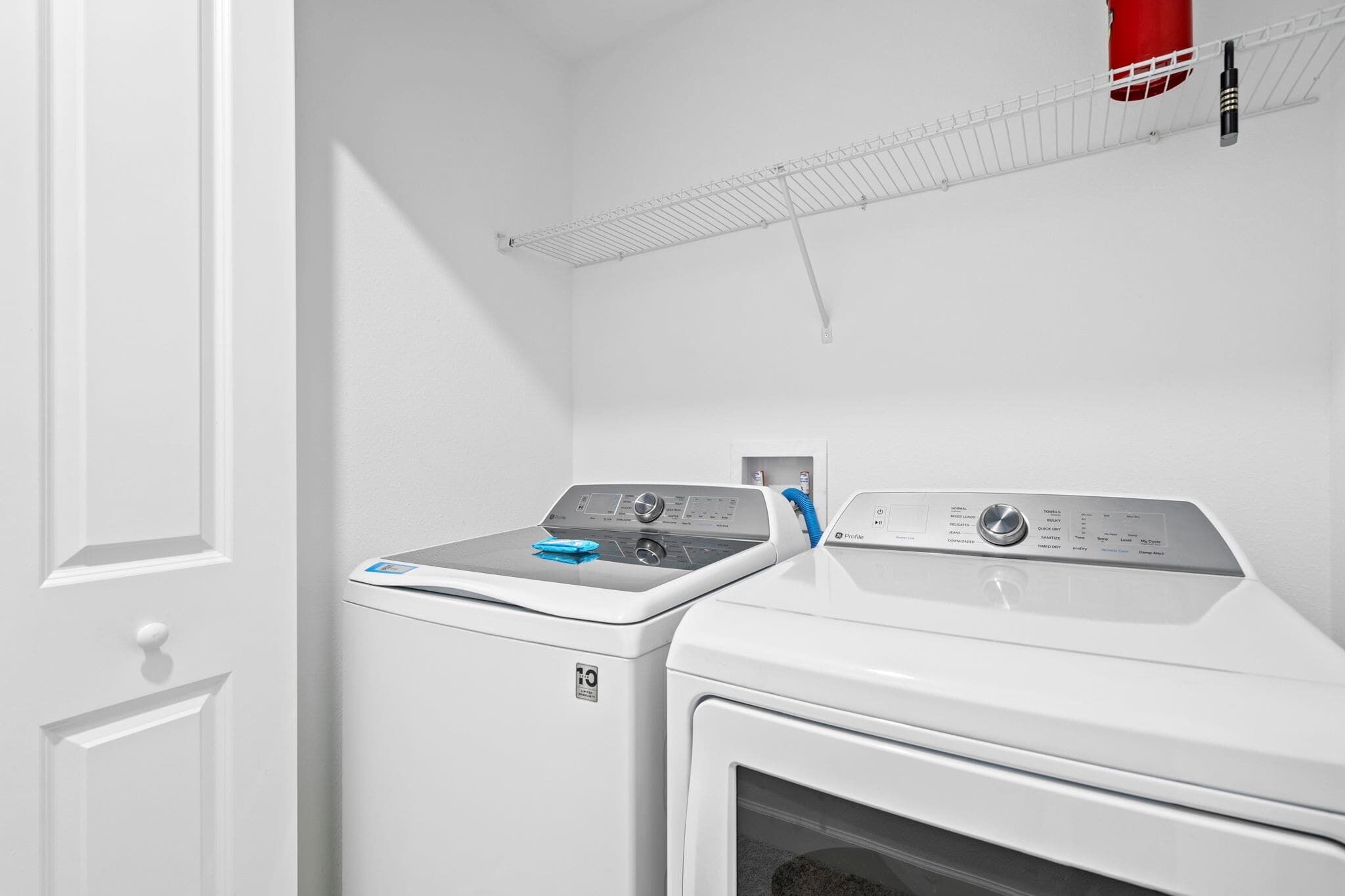 A laundry area with a front-loading washer and dryer, a drying rack, and a door.