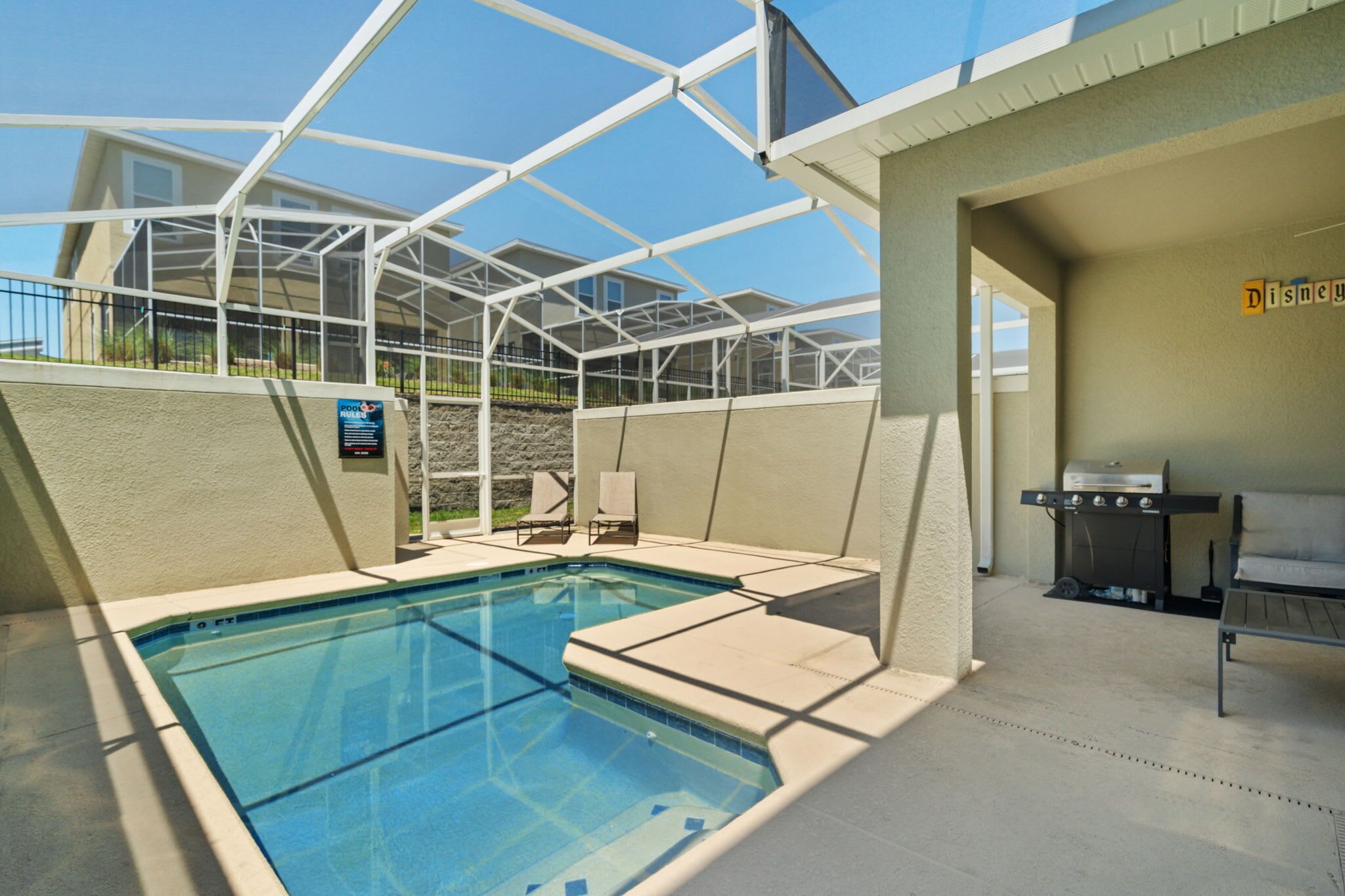 A pool area with a covered patio, a grill, and a sign that reads "Disney."