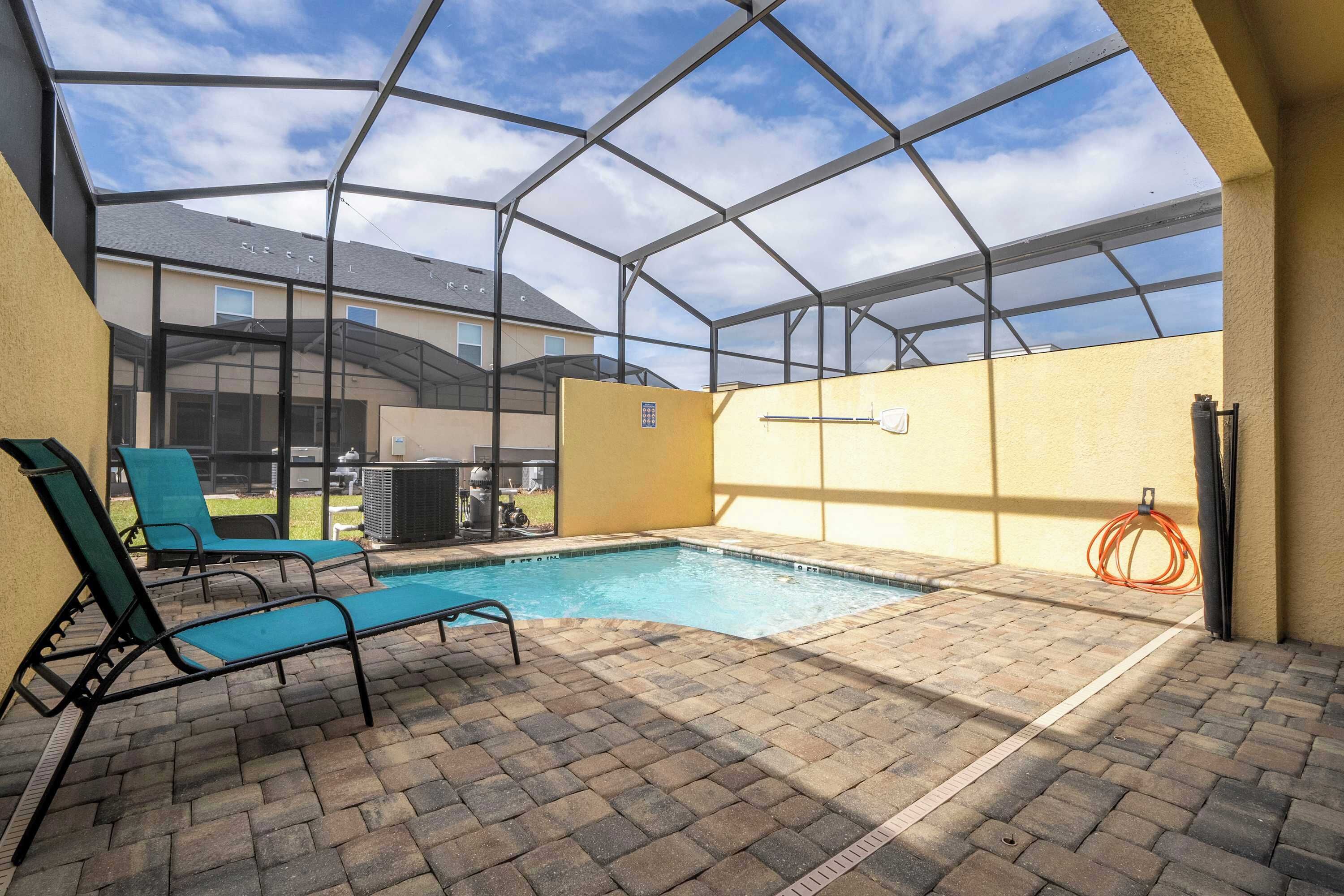 An indoor swimming pool with a glass enclosure, lounge chairs, and a brick floor.