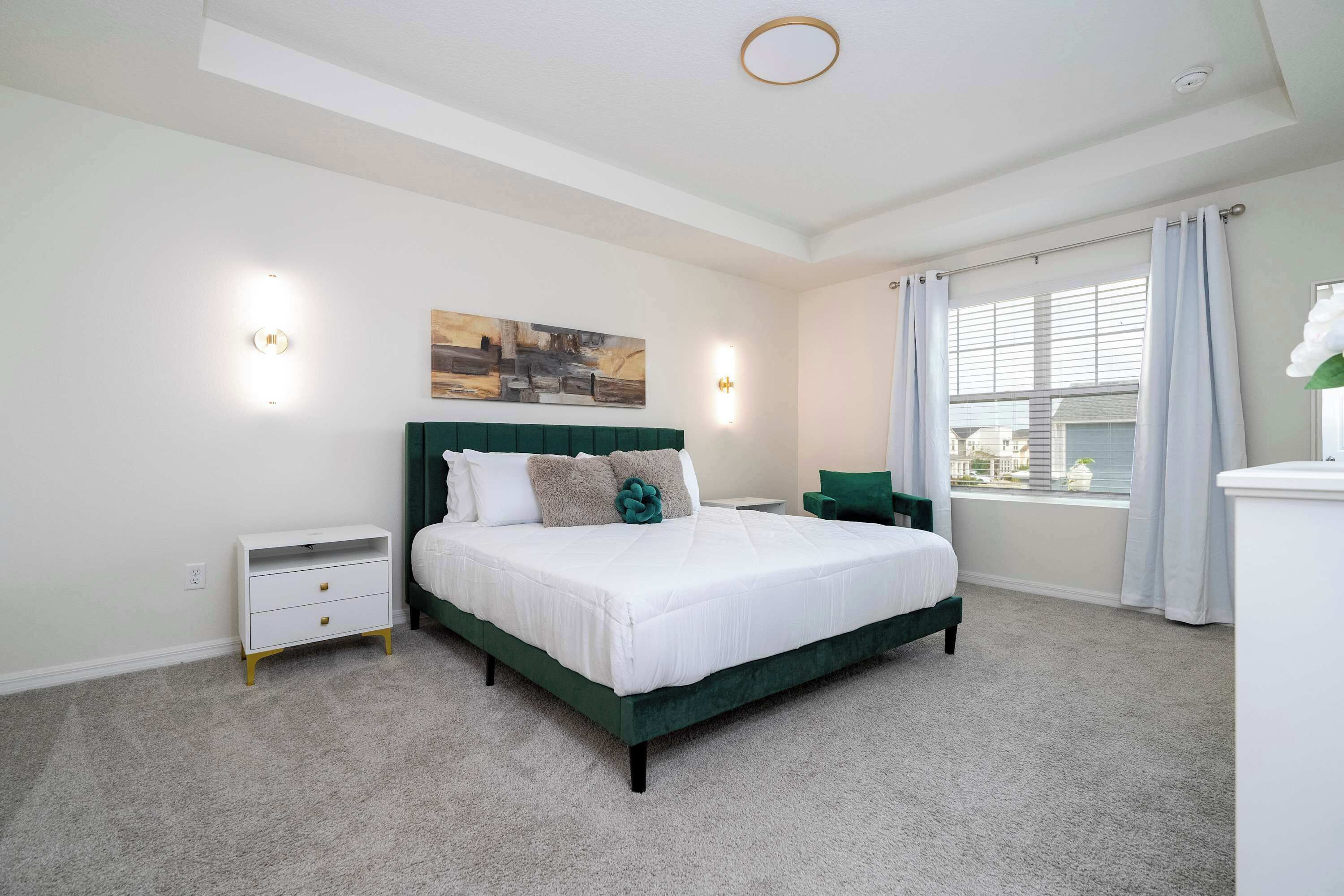 A bedroom with a bed, bedside tables, a window with curtains, and a painting on the wall.