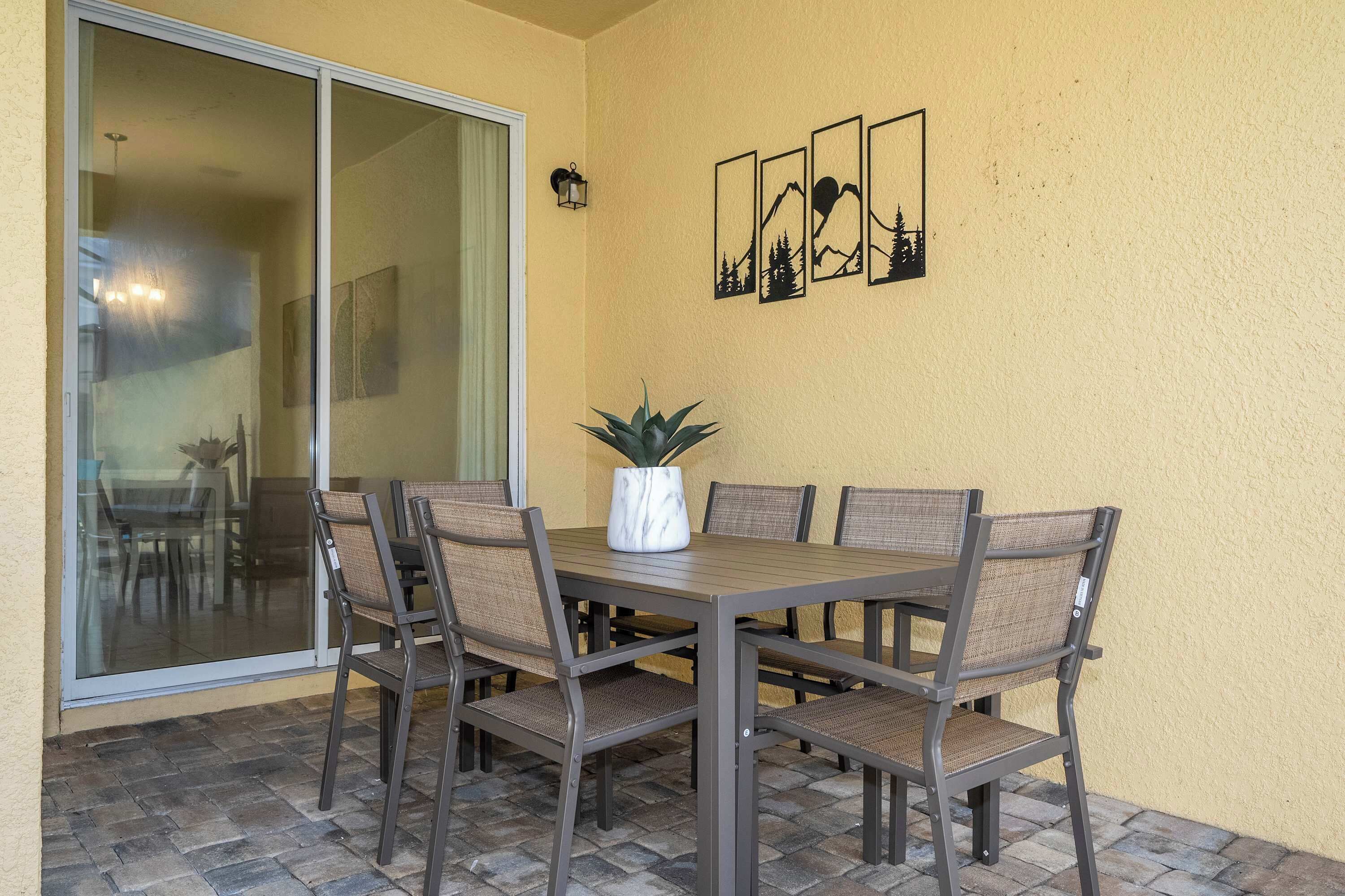 Comedor con mesa y sillas, una planta en maceta y un ventanal corredero que da a otra habitación.