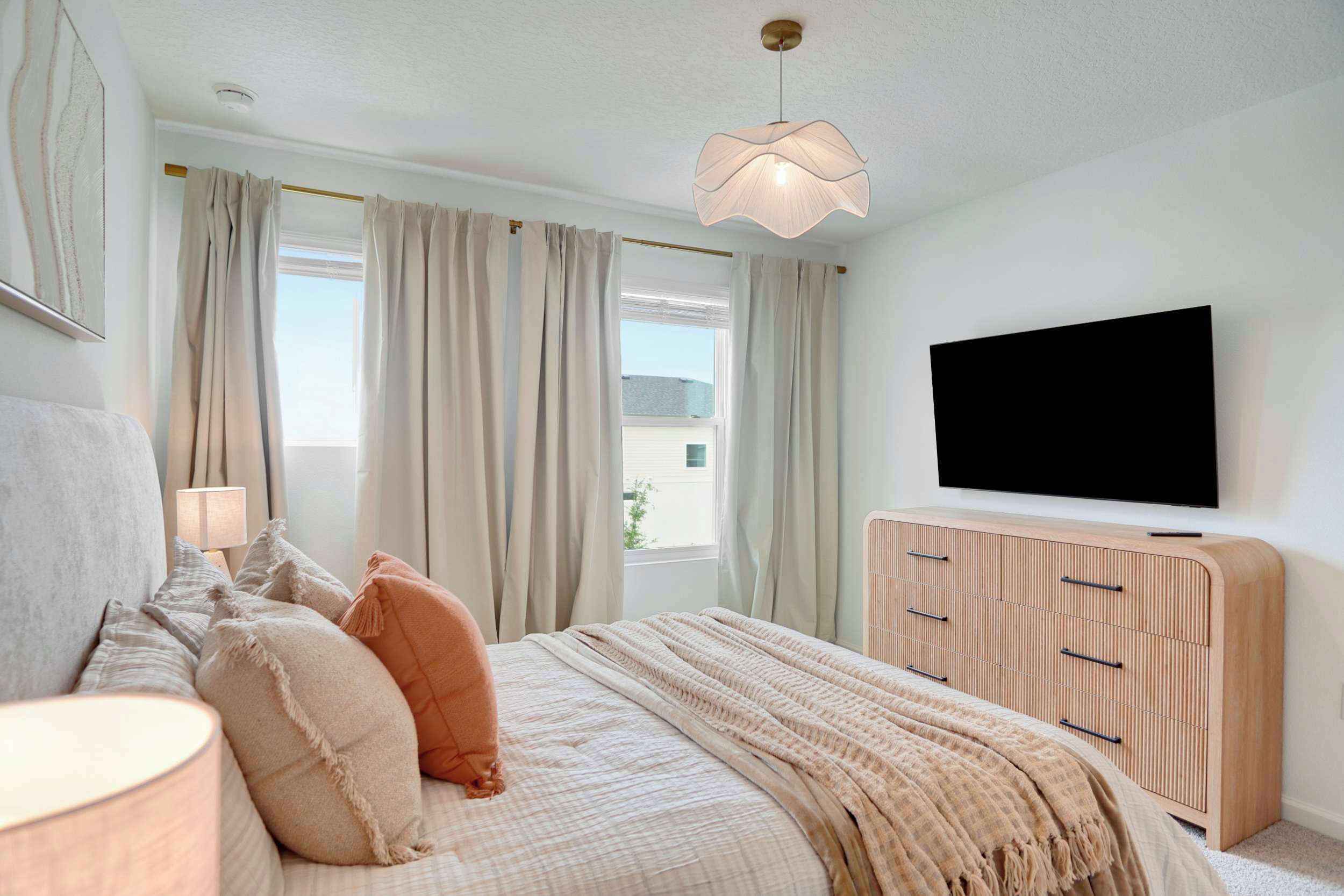 A bedroom with a bed, curtains, a TV, and a bedside lamp.