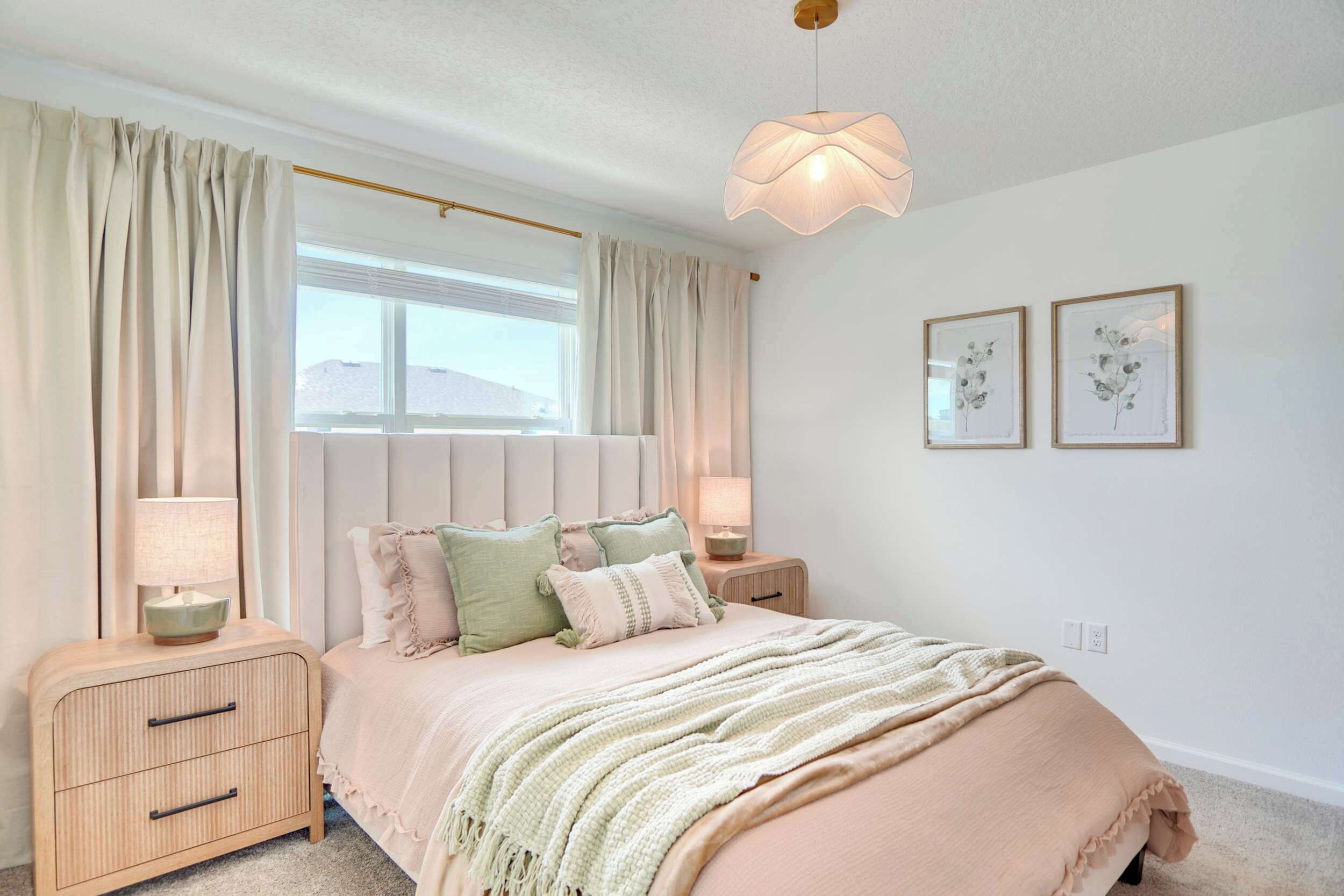 A bedroom with a bed, nightstands, a lamp, a window, and two framed pictures on the wall.