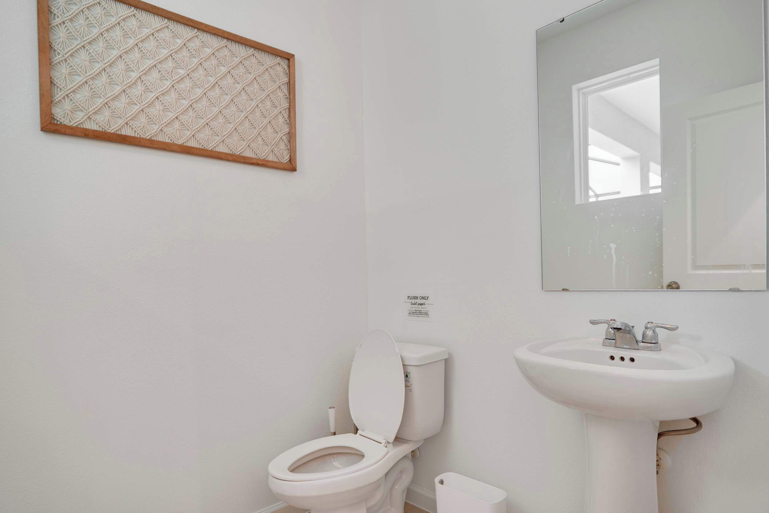 A white bathroom with a toilet, sink, and a decorative wall piece.