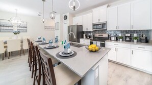A modern kitchen with white cabinets, a central island, and pendant lighting. - Chic, Spacious With Private Pool, Ideal Location (Kissimmee)