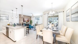 A modern kitchen with a central island, dining area with chairs, and a large window. - Chic, Spacious With Private Pool, Ideal Location (Kissimmee)