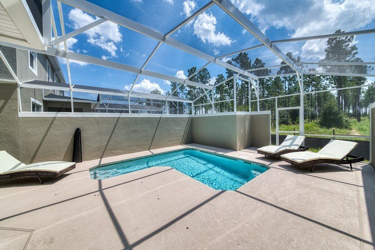 Una piscina cubierta al aire libre con sillas de descanso, cielo despejado y vistas a árboles.