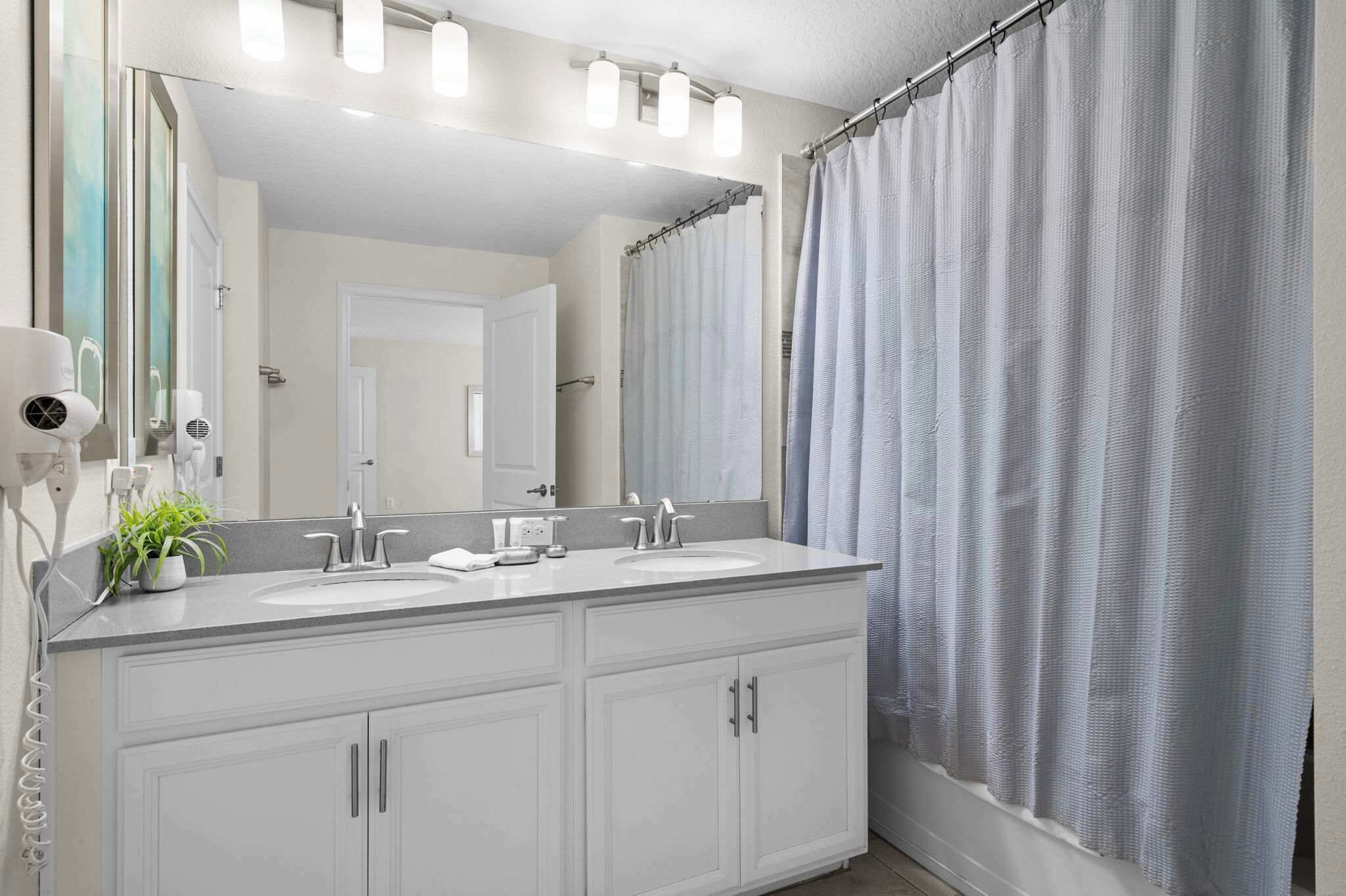 A bathroom with a double sink vanity, a large mirror, a hairdryer, and a shower curtain.