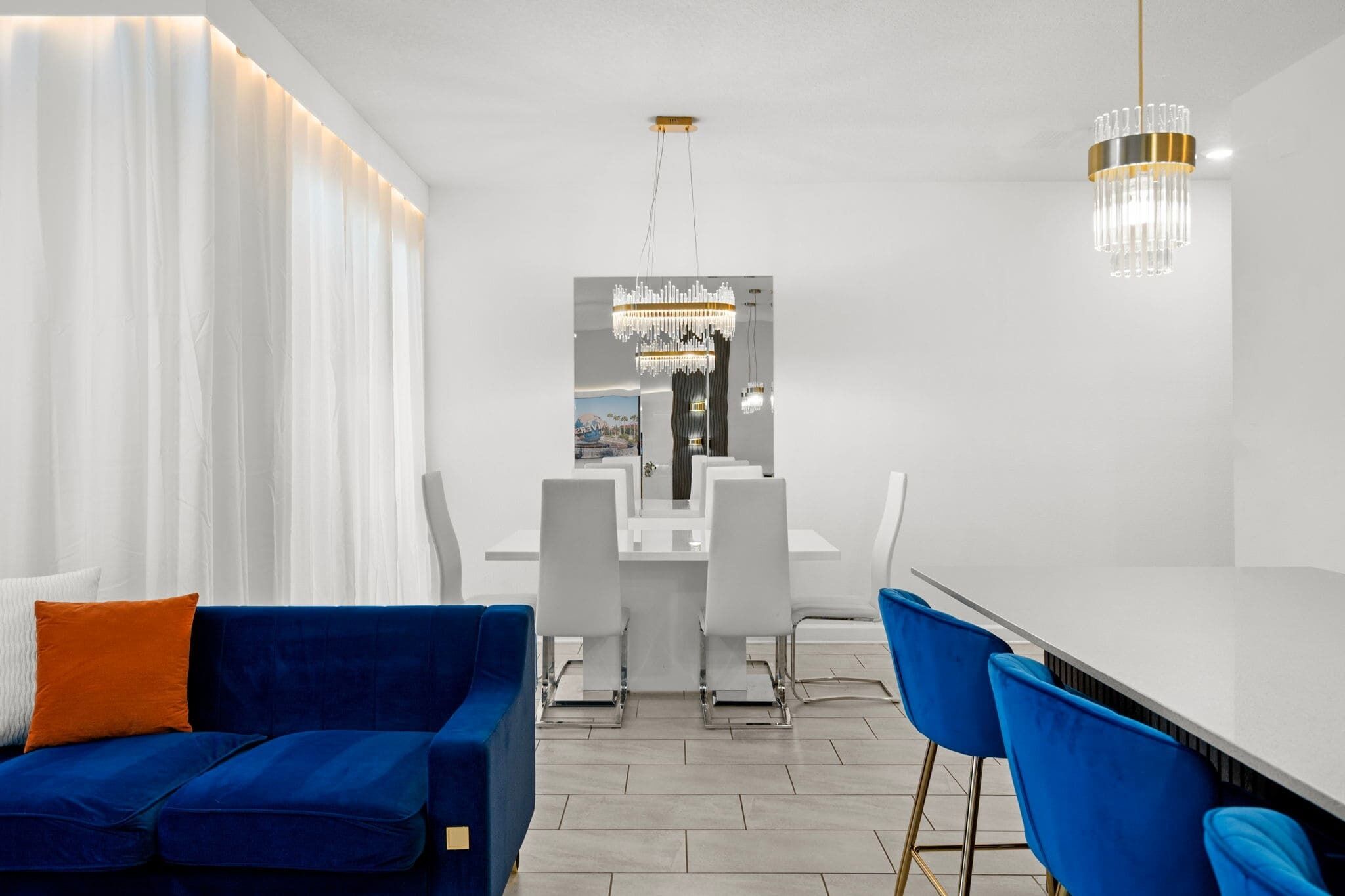 A modern dining area with a white table, blue chairs, and a chandelier.