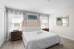 Een keurig opgemaakte slaapkamer met een bed, twee nachtkastjes, een schilderij aan de muur en een spiegel.