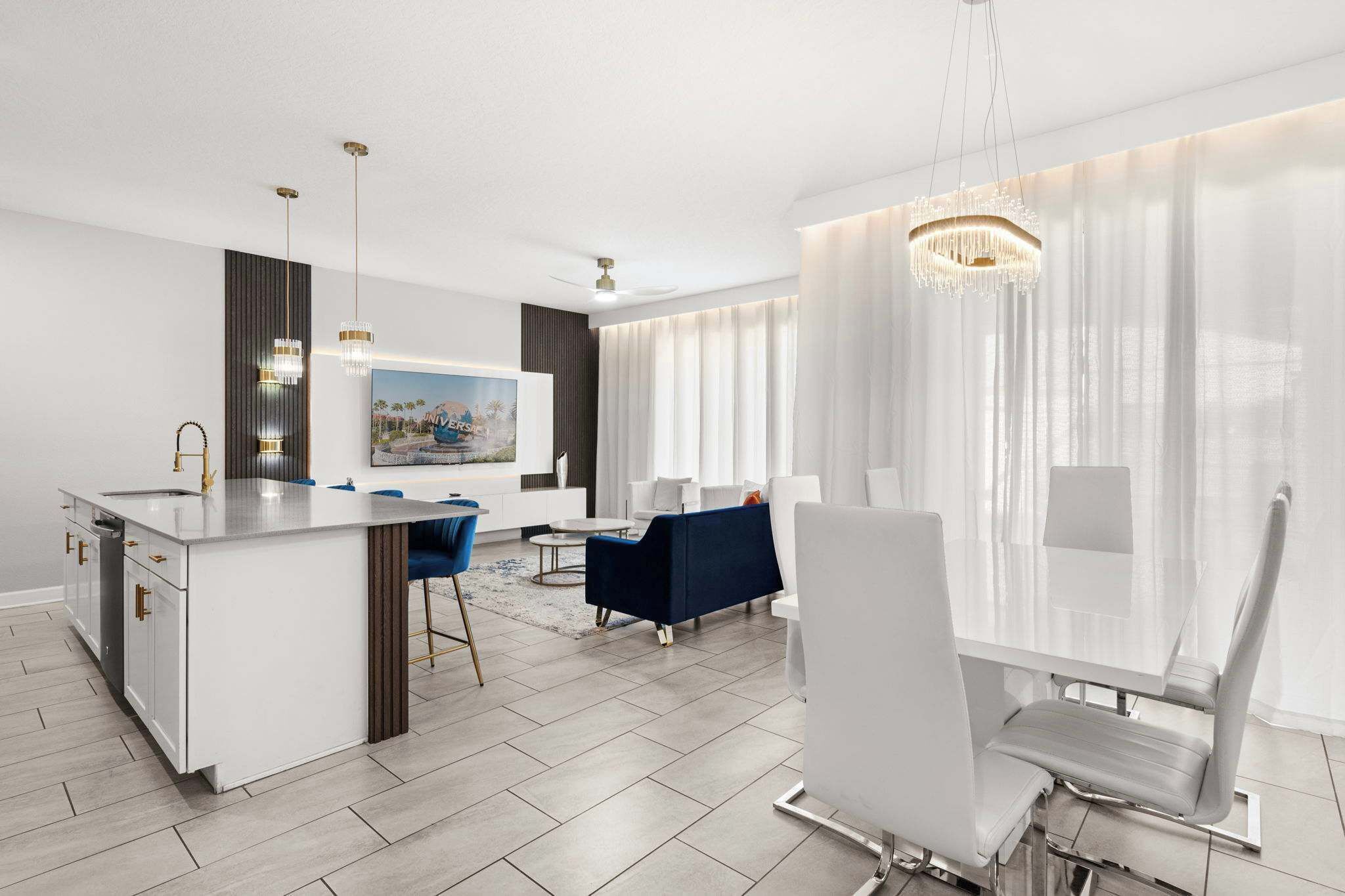 A modern kitchen with a central island, a dining area with a white table and chairs, and a living space with a sofa and a painting.