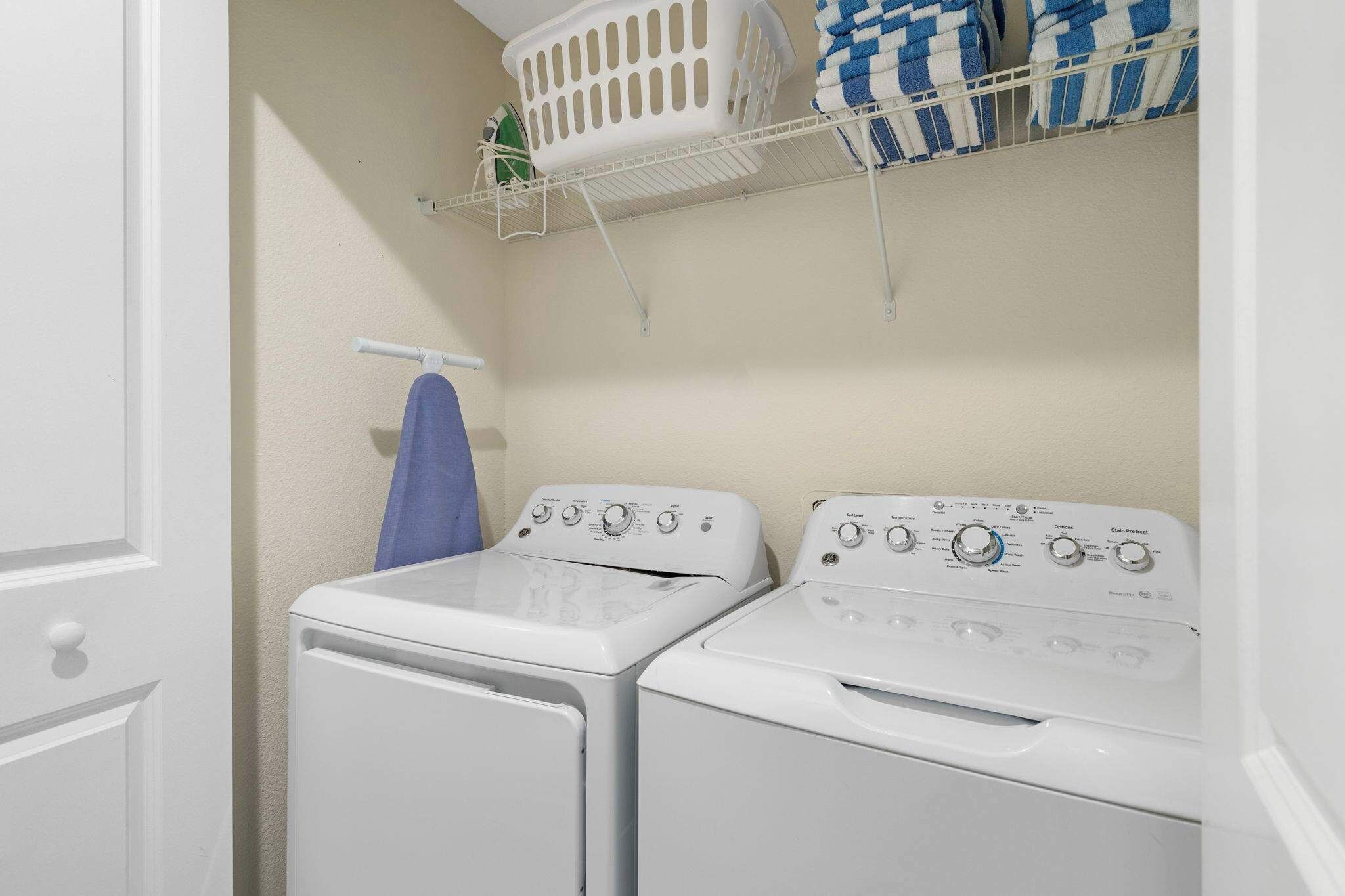 A laundry area with two washing machines, a drying rack, and a shelf with folded towels.