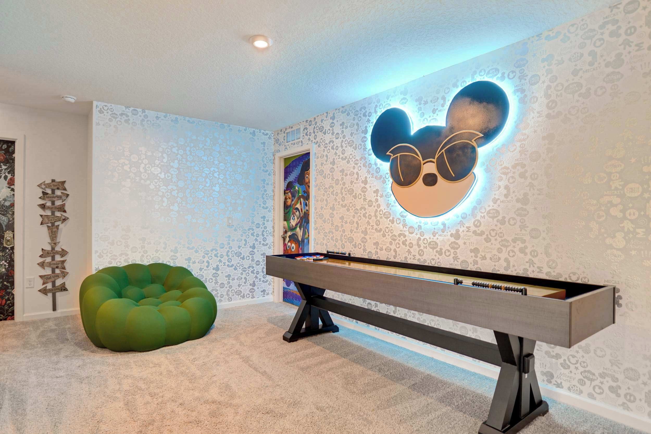 A room with a foosball table, a green bean bag chair, and a wall with a Mickey Mouse design.