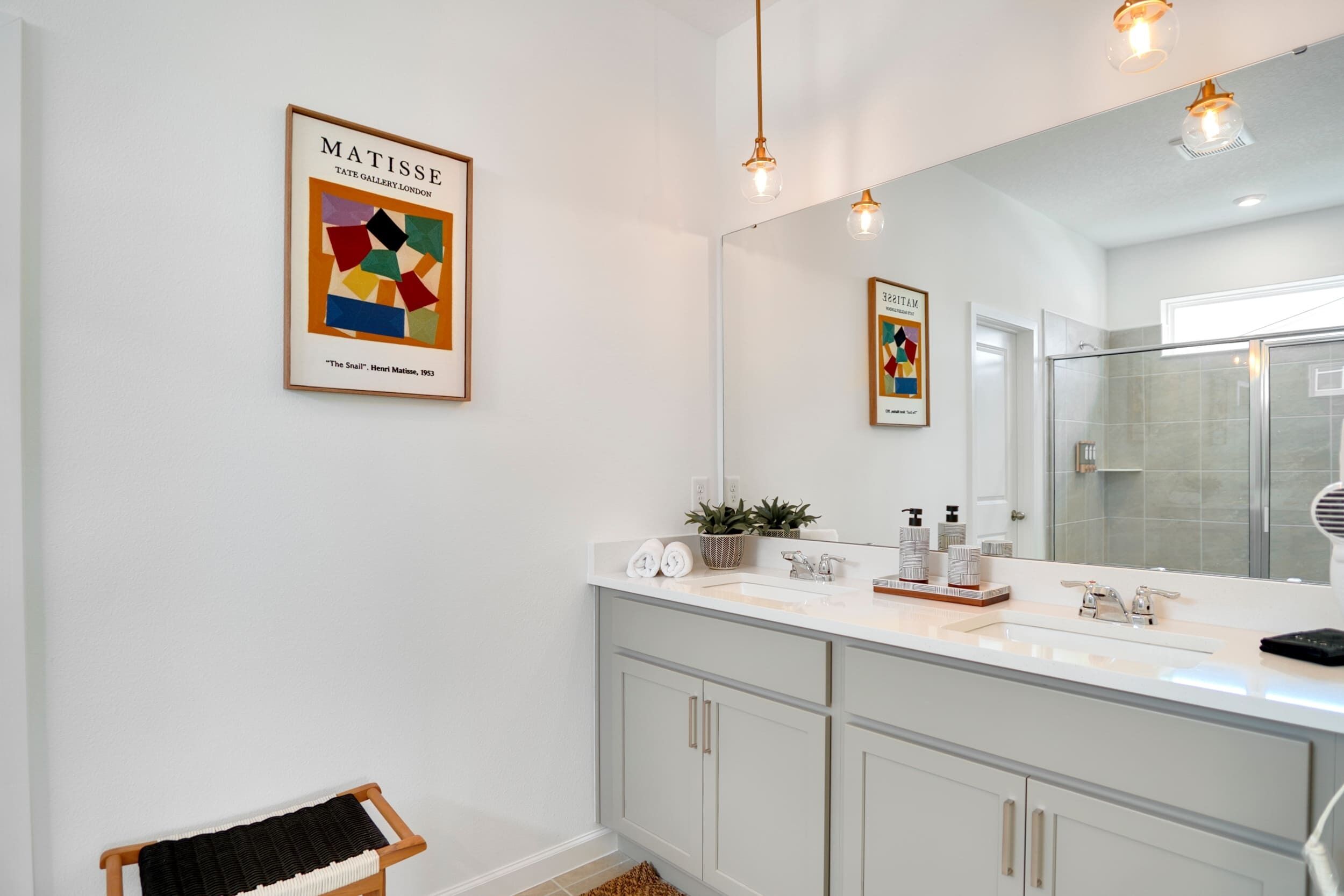 A modern bathroom with a large mirror, a framed artwork of Matisse, and a small stool.