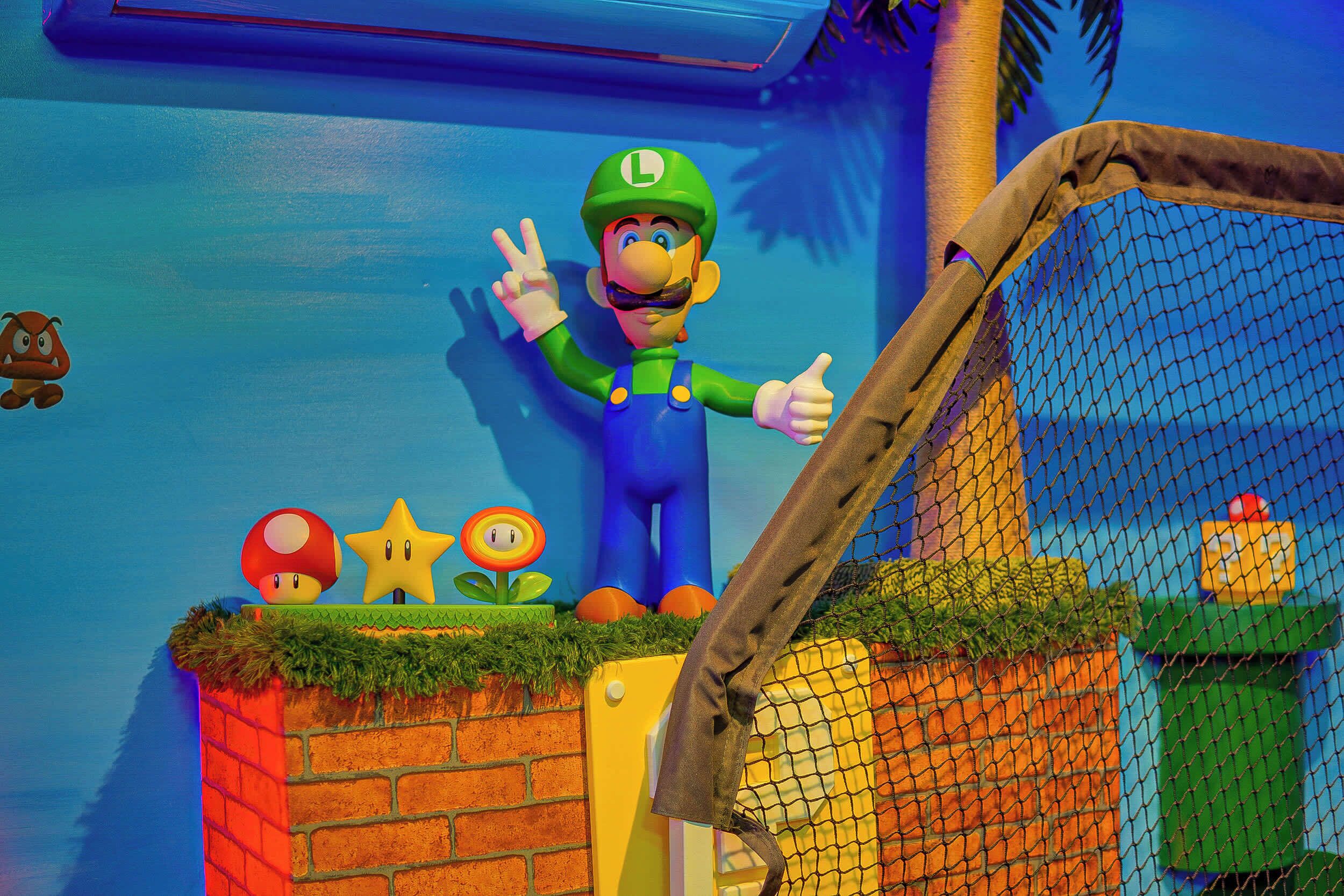 A Mario statue with a peace sign, a brick wall, a yellow door, and a netted area.