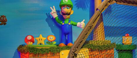 A Mario statue with a peace sign, a brick wall, a yellow door, and a netted area.