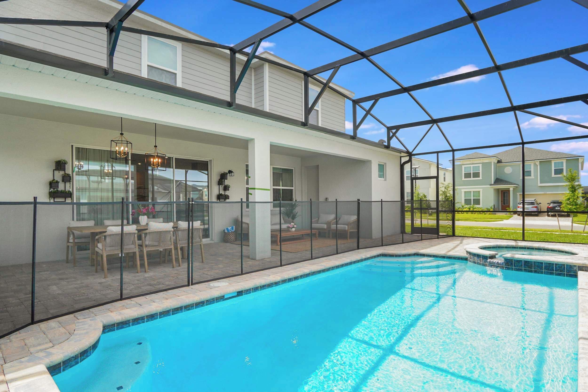 A swimming pool with a glass enclosure, a covered patio area with seating, and a view of neighboring houses.