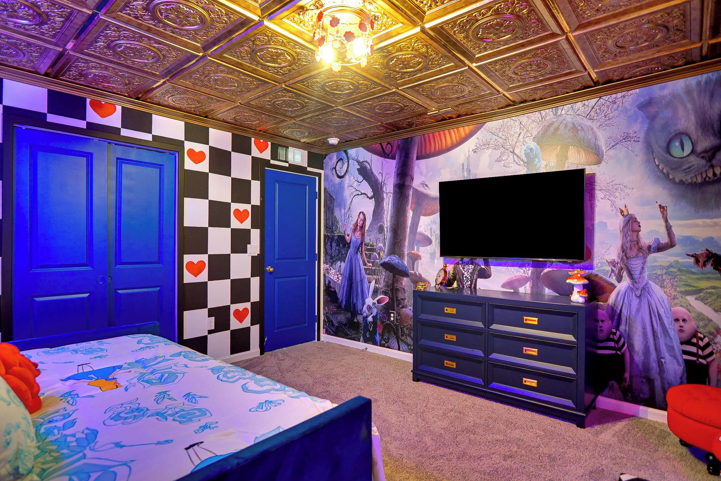 A room with a checkered wall, a large flat-screen TV, a dresser, and a bed with a blue canopy.