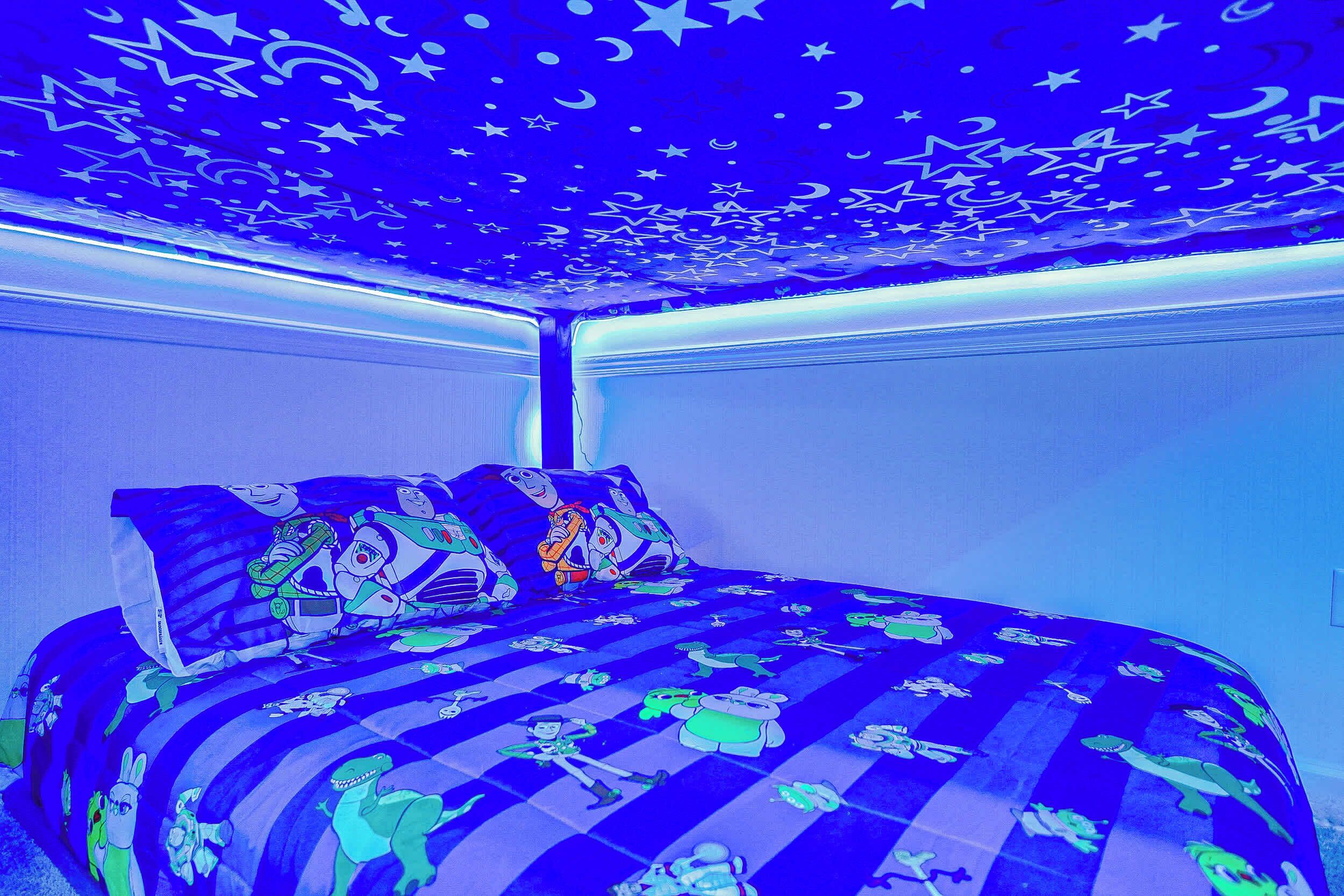 A bedroom with a bed featuring cartoon character prints, a starry ceiling, and a checkered bedspread.