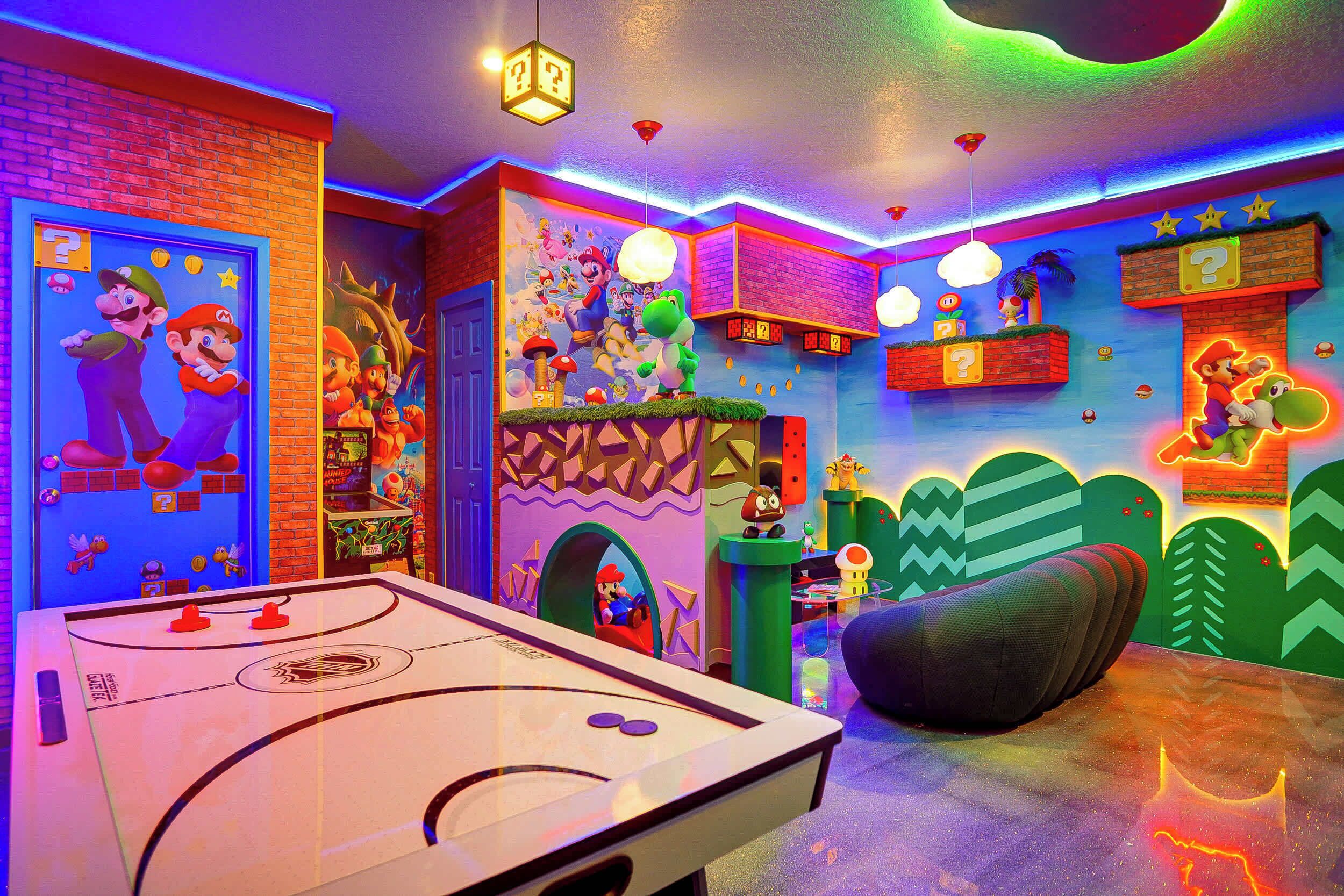 Une pièce lumineuse, avec un baby-foot, des illustrations de Mario et Luigi sur les murs, et un canapé vert.