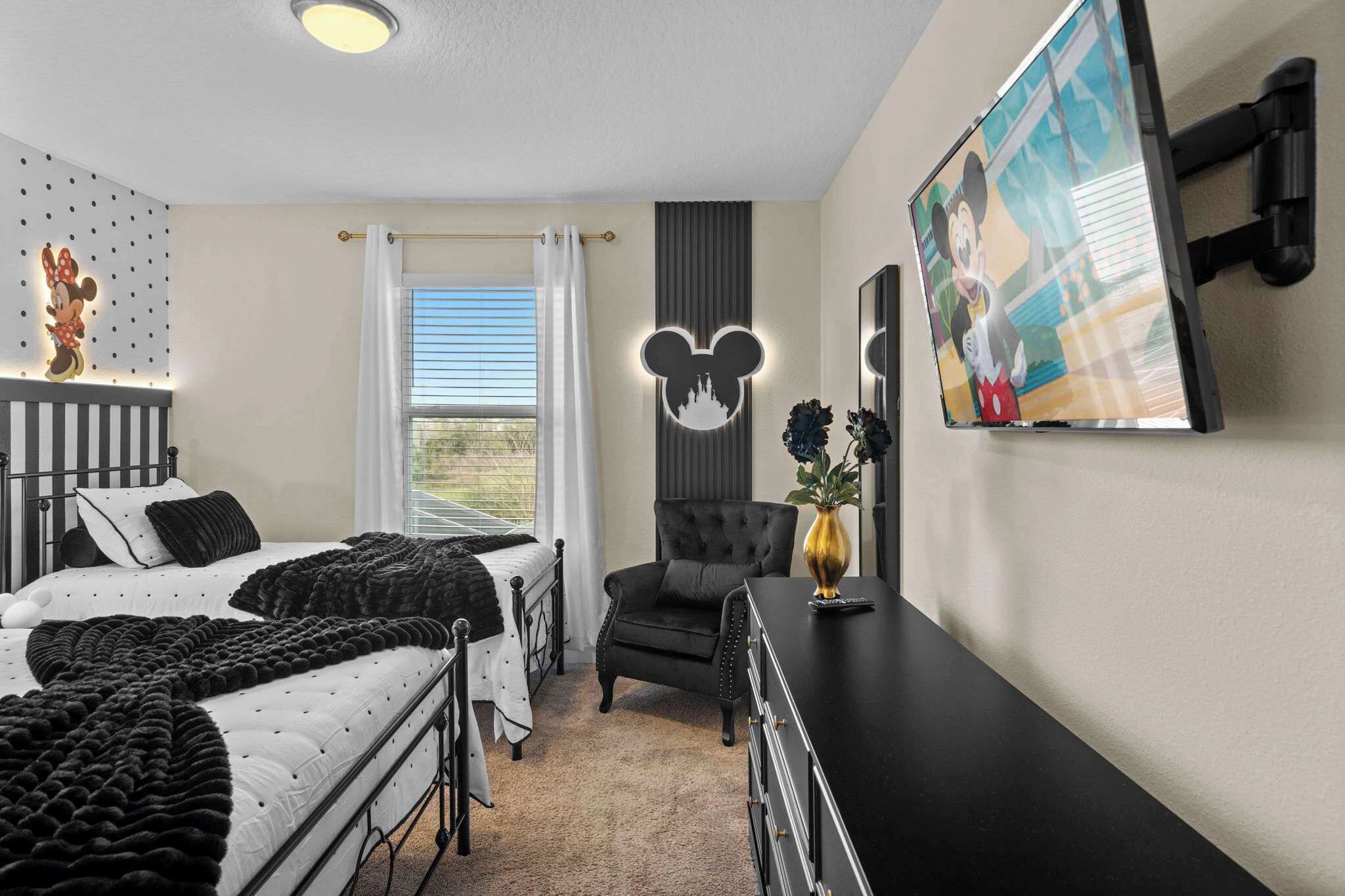 A bedroom with two beds, a desk, a chair, a TV, and a Mickey Mouse wall decoration.