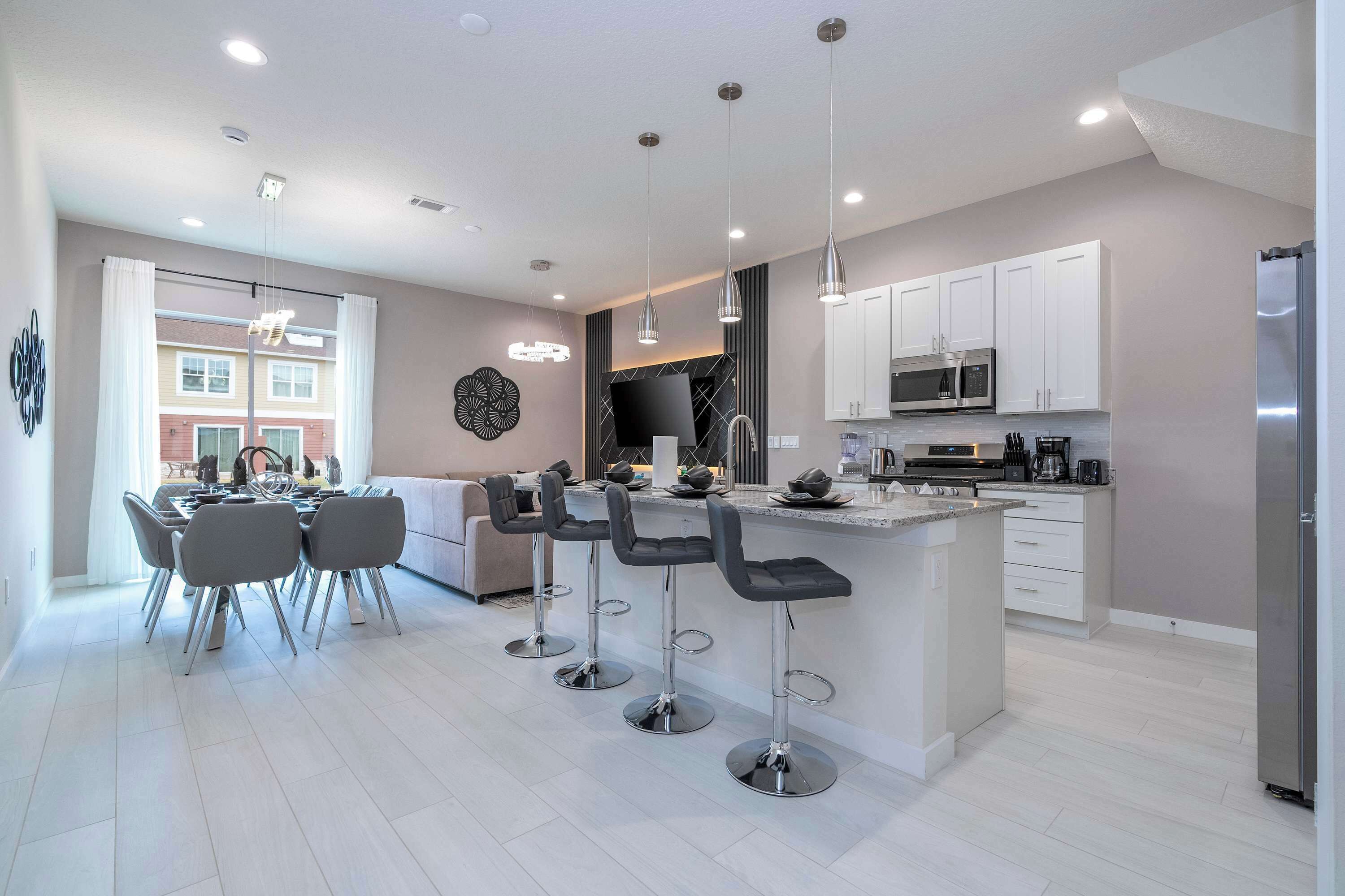 A modern kitchen with a central island, bar stools, and a dining area with a table and chairs.