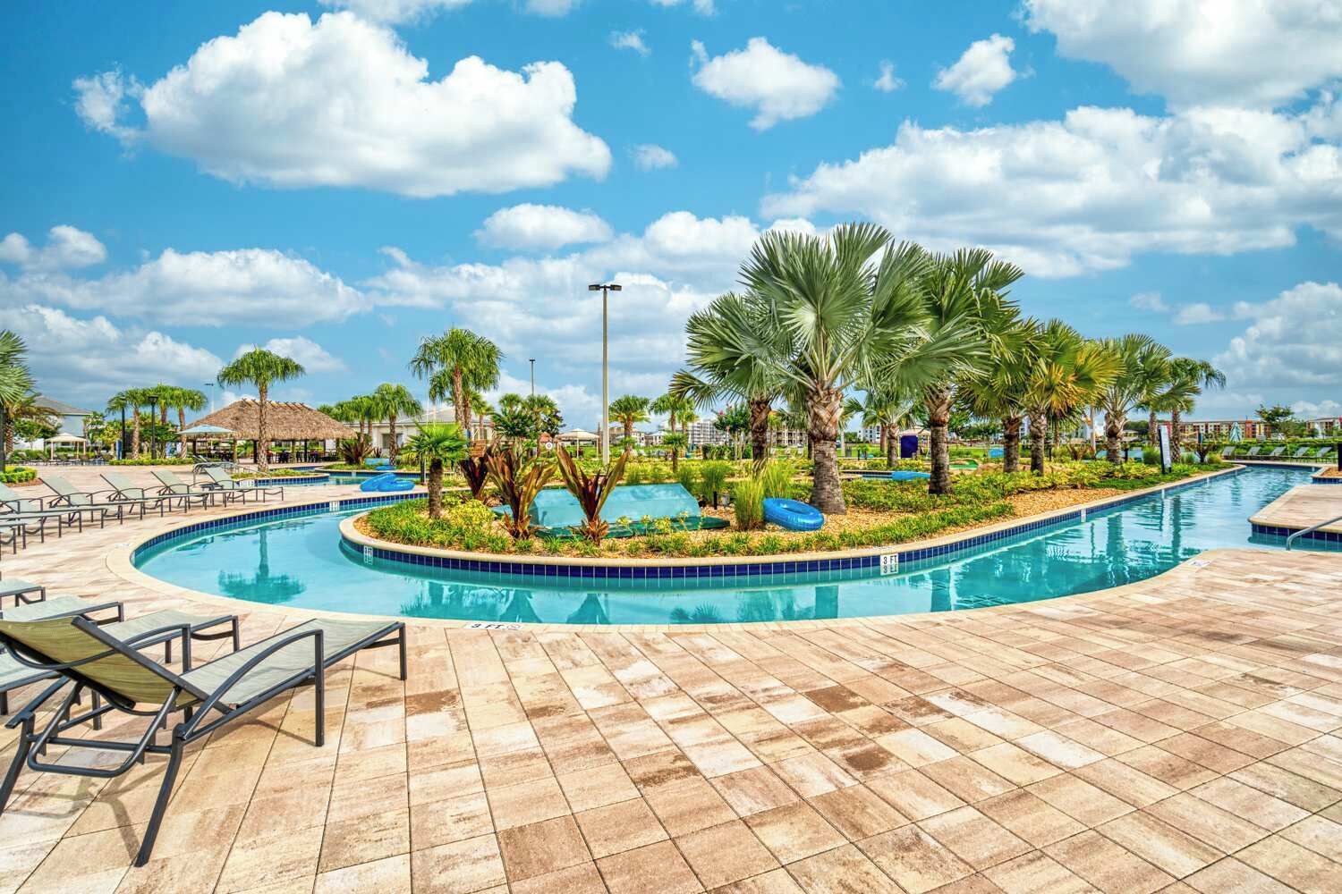 A swimming pool with palm trees, lounge chairs, and a tiled deck.