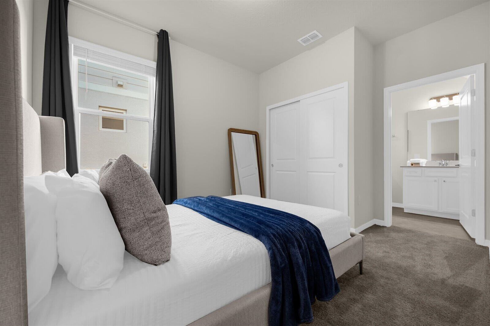 Een slaapkamer met een bed, een spiegel, een kledingkast en een badkamer met een wastafel en spiegel.